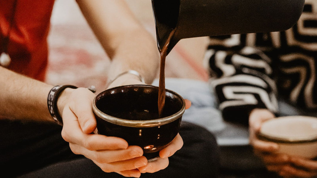 Zeremonieller Kakao wird in eine Tasse gegossen, die von einem jungen Mann gehalten wird