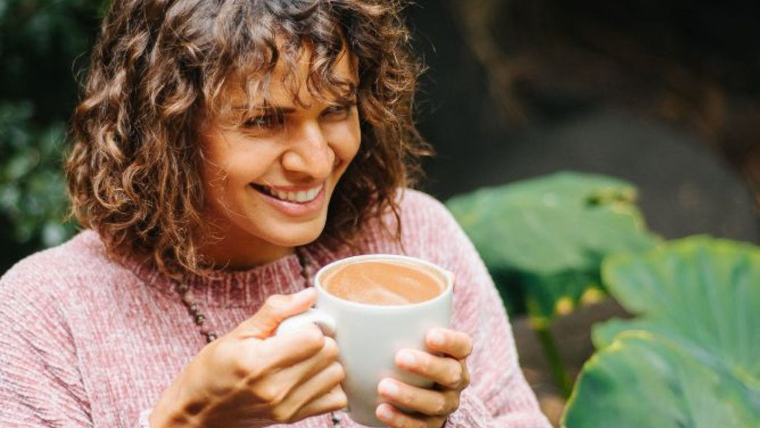Junge Frau trinkt lächelnd eine Tasse mit zeremoniellem Kakao